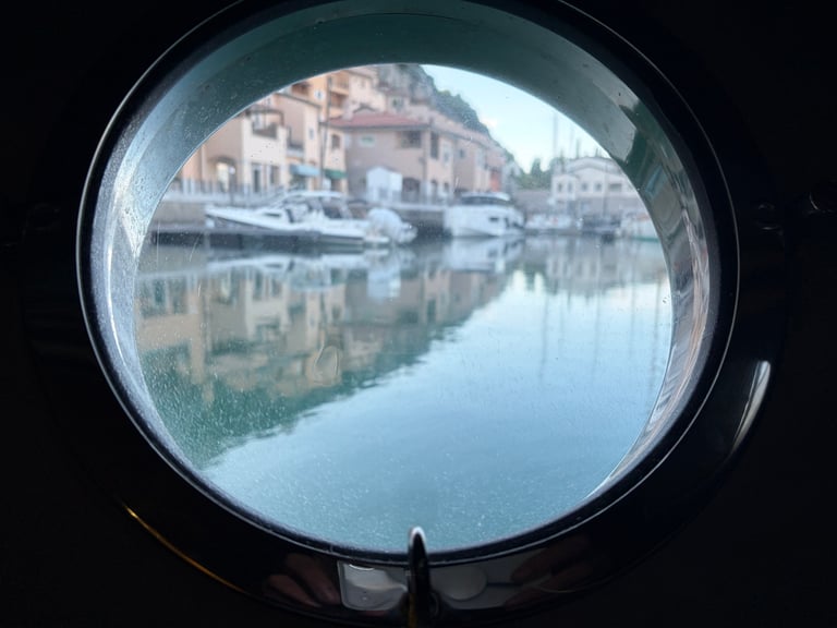 View through circular porthole of waterfront buildings and boats reflected in calm canal water